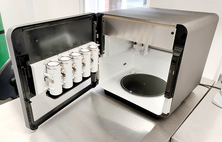 Foodini 3D food printer with open door, showing the food capsule holders and print tray
